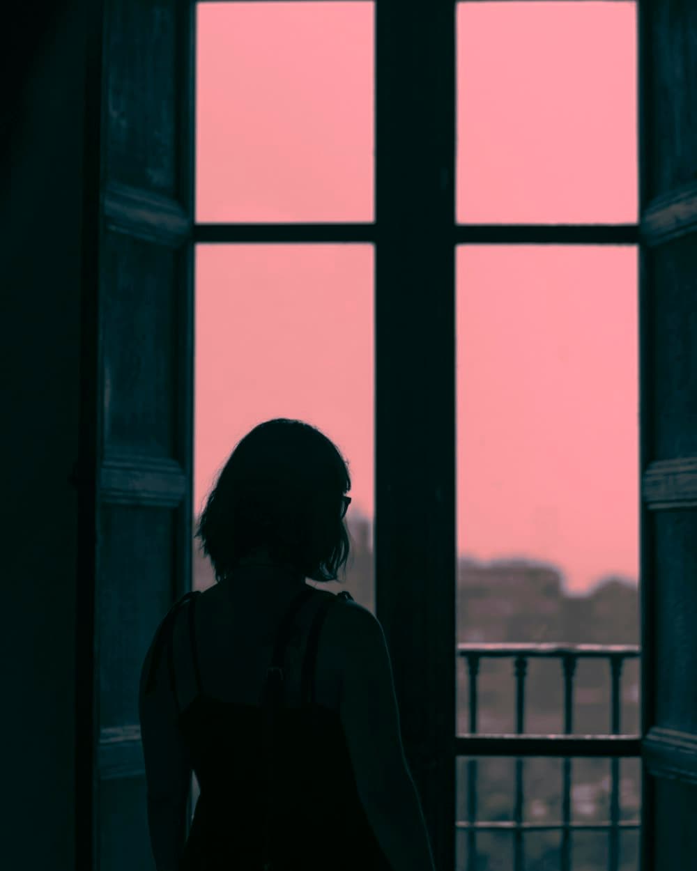 A woman standing at a tall window at dusk