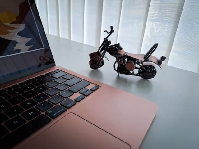A laptop on a desk next to a small model motorbike