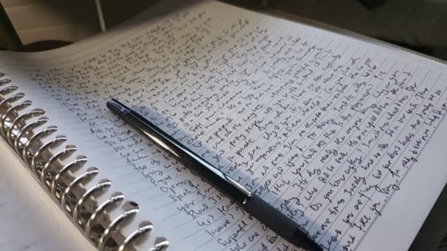A handwritten notebook page with a pen
